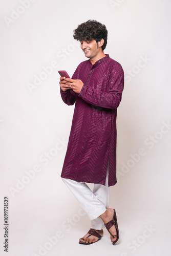 Young indian man wearing traditional kurta outfit using smart phone isolated on white background. Diwali celebration, Concept of festive sale, offer and discount. Online Shopping. Technology,