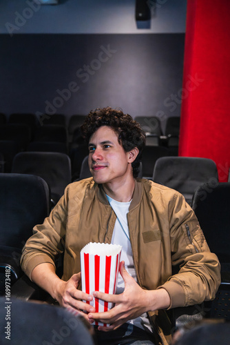 Billede på lærred Young man enjoying a bucket of popcorn while watching an exciting movie in a coz