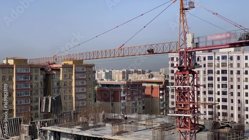 View of a construction crane at a high-rise construction site in the city. A group of construction workers is working on a high floor