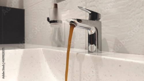 Water flows from a faucet in a modern bathroom, revealing brown liquid at a domestic residence during the afternoon
