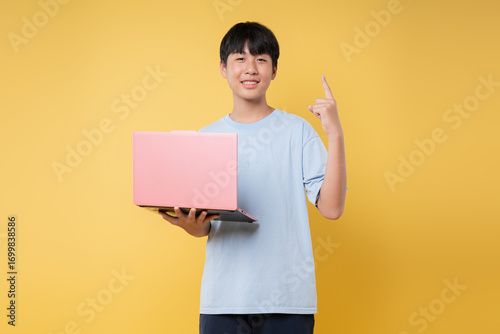 Enthusiastic student points upward with a pink laptop against vibrant yellow showcasing an idea