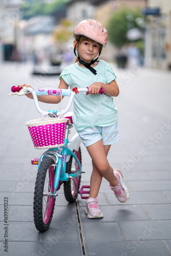 Cute girl wearing cycling helmet and riding bike at park. Portrait of a playful funny girl in a pink safety helmet on her bike