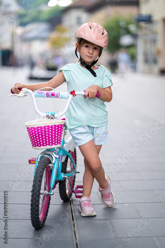 Cute girl wearing cycling helmet and riding bike at park. Portrait of a playful funny girl in a pink safety helmet on her bike