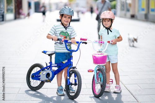 Two confident youngsters enjoy a bike ride in the city, showcasing their friendship and joy. The image highlights health and the importance of safety measures like wearing helmets. 