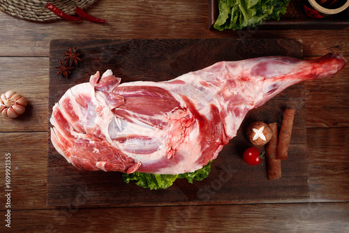 Raw Lamb Leg with Fresh Herbs and Spices on Rustic Wooden Board for Cooking Preparation