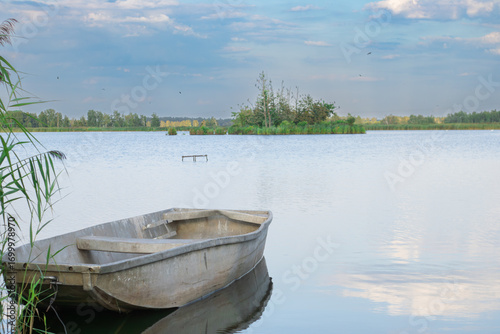 Old wooden boat on the shore of a calm lake surrounded by nature. Scenic lake landscape with a rustic wooden boat in natural light, perfect for travel, tourism, nature, and relaxation projects.