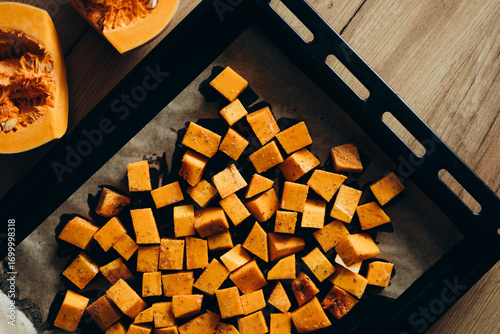 Pumpkin cubes in spices on the tray, prepared to bake, top view.