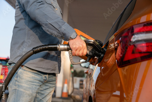 Close-up of a Man refuelling orange car at gas fuel station. Male filling diesel at petrol station using a fuel nozzle