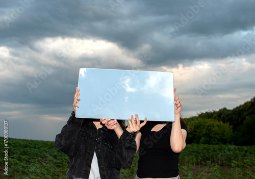 Two women holding a mirror that reflects the sky	