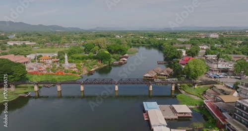 Aerial View of Iconic Bridge Over River Kwai in Kanchanaburi Surrounded by Lush Greenery, Vibrant Buildings, and Serene Waters