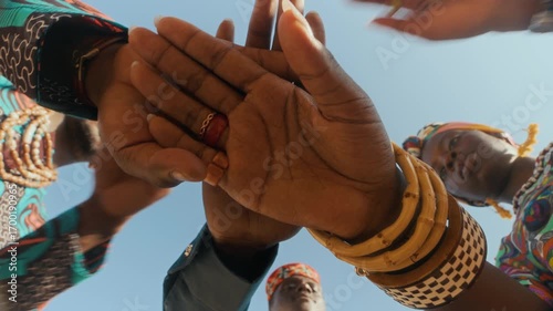 From below view of three young Black people in ethnic clothes joining their hands, symbolizing unity and solidarity