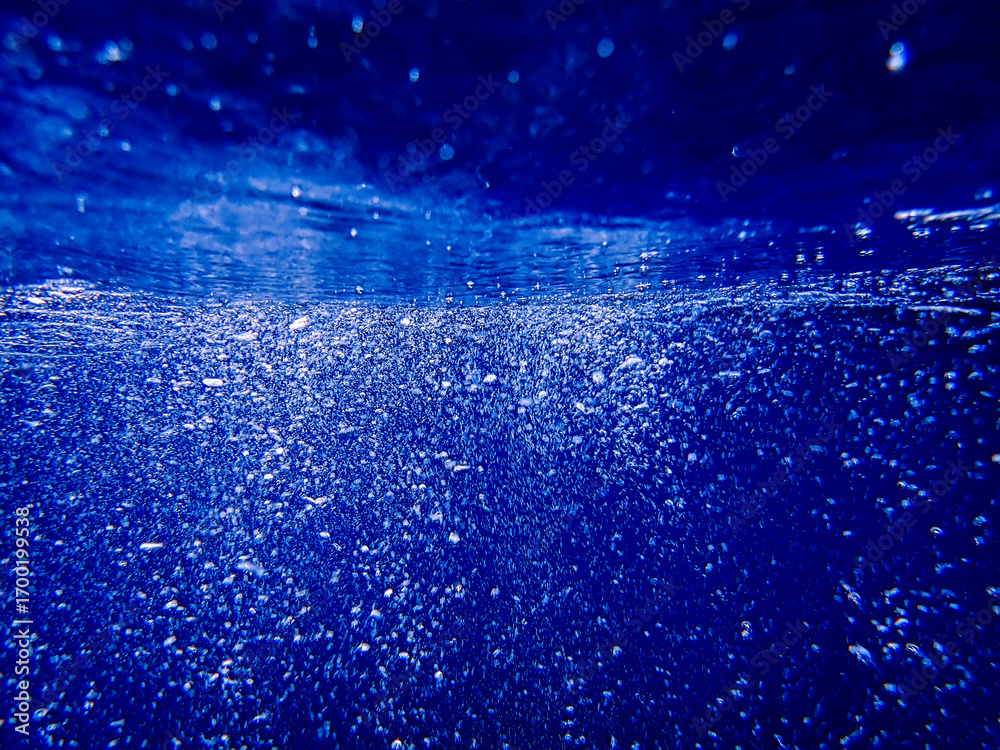 Fototapeta premium Underwater photography of the deep ocean with the ocean surface rippled with bokeh, bubbles, and lens flare great for water background with room for copy, Sunlight underwater with air bubbles rising.