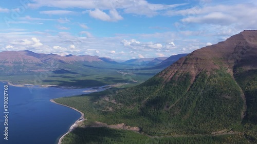 Summer panorama shows Lake Lama deep water, curving shore and basalt ridge on the Putorana Plateau. Bright weather opens a long valley to the horizon, ideal for tourism, documentary and branding