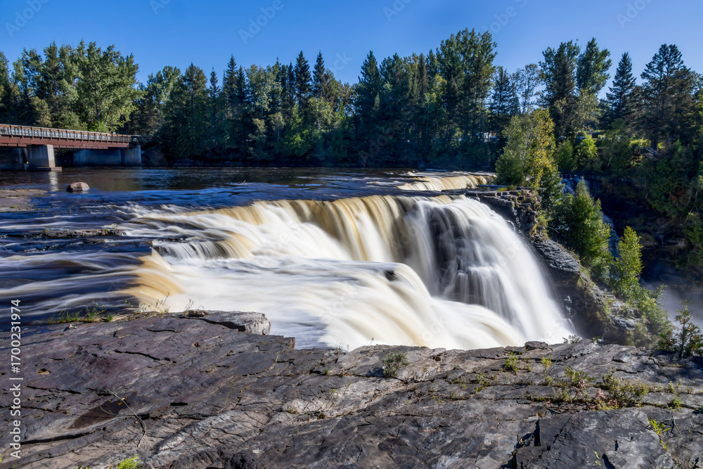 Obraz premium Kakabeka Falls, Ontario's stunning natural wonder, cascades powerfully through lush forests, offering mesmerizing scenic views and a serene escape into nature's beauty.