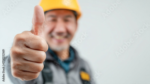 Man in yellow hard hat giving thumbs up with blurred background in a studio setting indoors