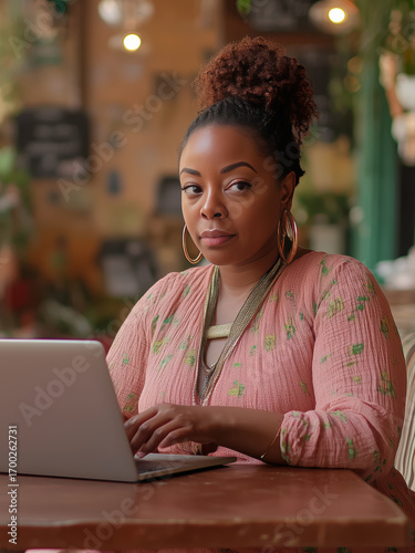 Young black serious concentrated woman sits at a table in a cozy cafe and works on her laptop online remotely as self employer or freelancer