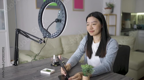 Young Thai woman recording a beauty video vlog at home. She talks to the camera with confidence while applying makeup and sharing skincare tips.