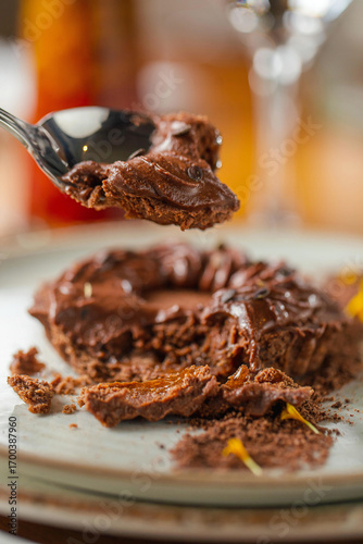 Close-up of a rich chocolate dessert on a plate, with a spoon lifting a portion of creamy chocolate mousse, decorated with chocolate shavings and small edible flowers.