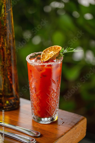 A classic Bloody Mary cocktail served in a crystal glass with salted rim, ice cubes, and garnished with a dried lime slice and fresh parsley, set on a wooden table.