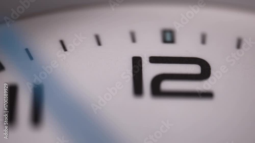 Clock face with number 12 close-up, blurred second hand slowly moving over the numerals.