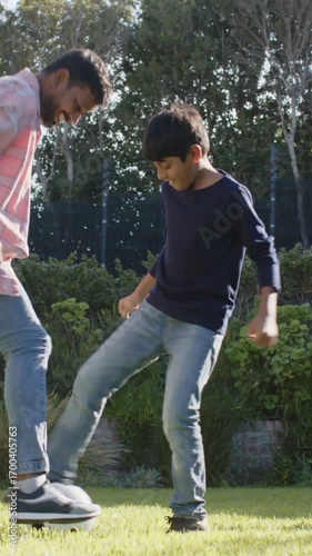 Playing Indian father and son kicking soccer ball on backyard lawn, with black-and-white ball