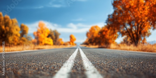 clear day with a long, empty road stretching into the distance, with the background a vibrant, out-of-focus blur of autumn trees