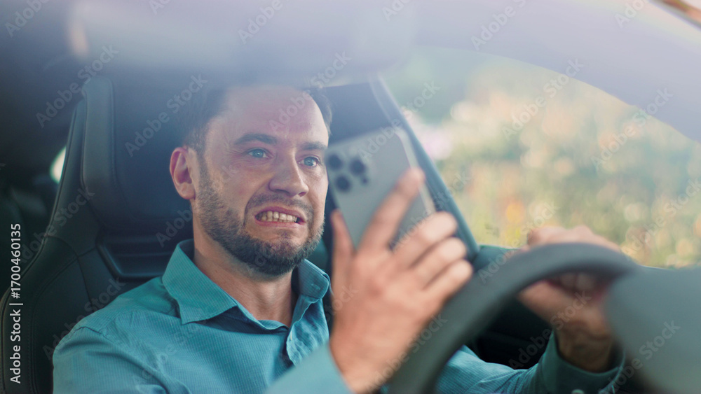 Obraz premium A distracted driver is using a mobile phone while driving, highlighting safety concerns. Man driver demonstrates significant frustration as they engage with a smartphone while driving on the road