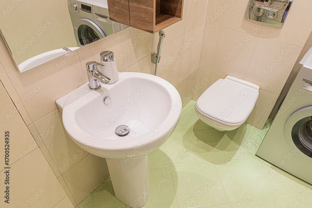 Fototapeta premium A clean bathroom with a white pedestal sink, toilet, and washing machine. Light green tiles
