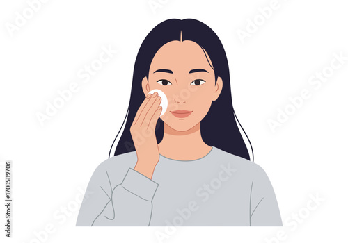A woman is cleansing her face with a white cotton pad in front of a white background