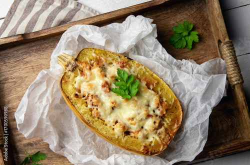 Spaghetti squash or vegetable spaghetti stuffed with minced meat and cheese, served in its shell. Homemade dish on a rustic wooden background.