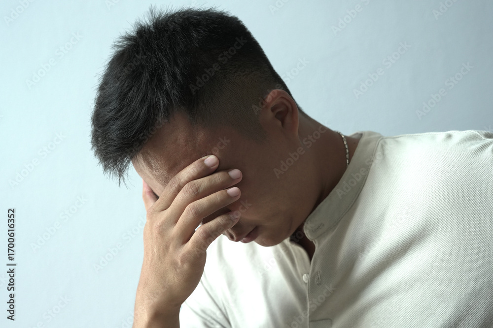 Fototapeta premium An asian businessman is suffering from headache, tension from forehead and getting stress and depression during working, massaging his head, employee life office stress and office syndrome concept. 