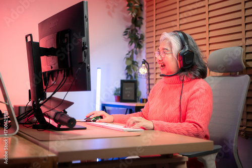 Senior woman gamer wearing headphones and playing on a desktop computer in a colorful gaming setup