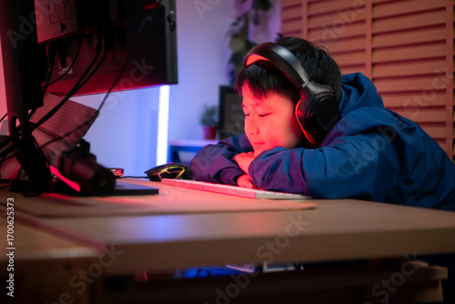 A boy gamer wearing headphones and playing on a desktop computer in a colorful gaming setup