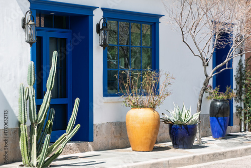 Historic downtown Tucson adobe house with Blue Doors and Windows. Large planters in yellow and blue line the front walkway. A tall cactus is prominent in the foreground. Pima County, Arizona, USA.