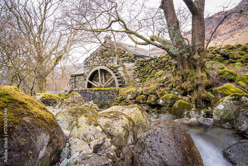 Old stone mill building with wooden waterwheel and mossy stream in Lake District