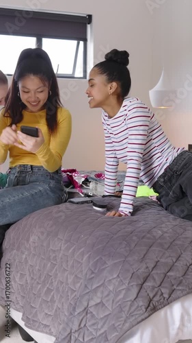 Vertical video: Diverse friends swiping phone for styles, comparing pink top on quilt in bedroom