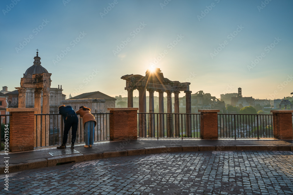 Naklejka premium Tourist couple visit Temple of Saturn at Roman forum ruins onsunrise in Rome. Italy