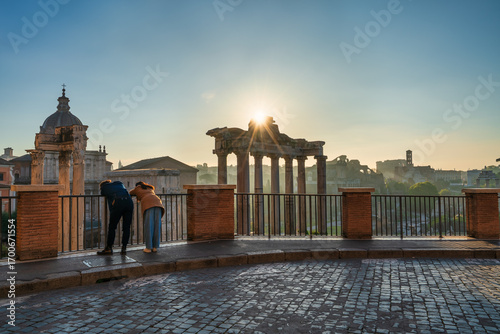 Tourist couple visit Temple of Saturn at Roman forum ruins onsunrise in Rome. Italy