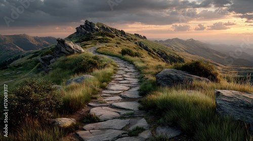 Fototapeta Naklejka Na Ścianę i Meble -  Stone paved path winds through a grassy mountain ridge under dramatic sky at sunset in Bieszczady National Park, Poland