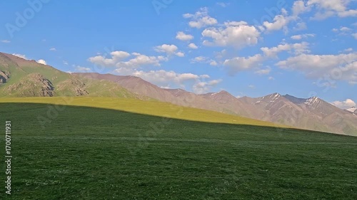 green foothills and mountain range in the background under blue sky at summer evening in Kyrgyzstan