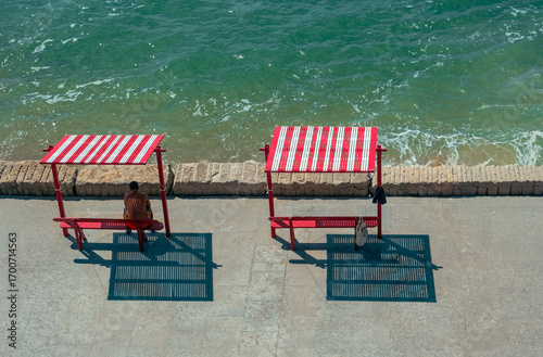 Man Sitting Under Red Striped Shade by the Sea