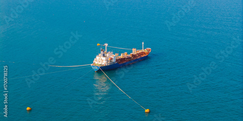 Tanker oil ship anchored in vibrant blue waters, aerial top view