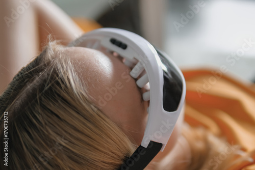 Gen Z woman unwinds  home smart eye massager?wellness tech  recovery, mindfulness and stress relief. Cozy greenery and soft light set a self-care, digital-detox mood, promoting balance, calm wellbeing