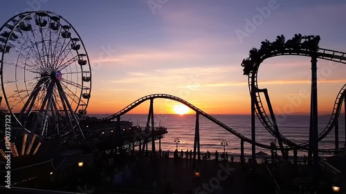 Stunning Sunset at an Amusement Park Pier with Ferris Wheel and Roller Coaster in Motion over the Pacific Ocean
