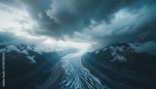 An epic aerial view captures a vast glacier winding through dramatic, cloudshrouded mountains under a stormy sky