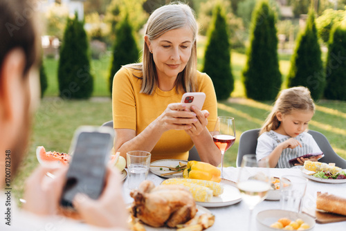 Принти на полотні Family using smartphones during lunch in garden