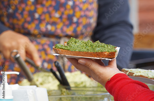 Fotografia Woman holding a fresh slice of bread with basil pesto spread just bought at the farmers market at Naplavka in Prague