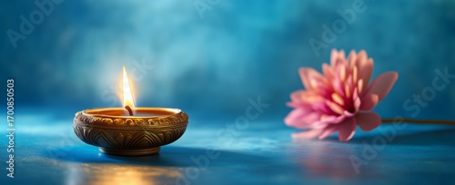 Decorative Diya Lit Beside a Pink Flower on a Serene Blue Background.