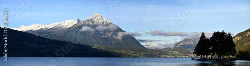 Foto The Serene Thun Lake Surrounded by Snow-Capped Peaks Under a Clear Blue Sky
