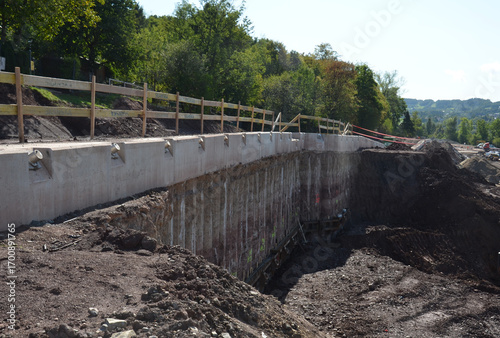Construction site with ground stabilization works, including retaining wall, piling, soil nails, and steel reinforcements. Heavy machinery in use to secure a landslide area with engineering solutions 